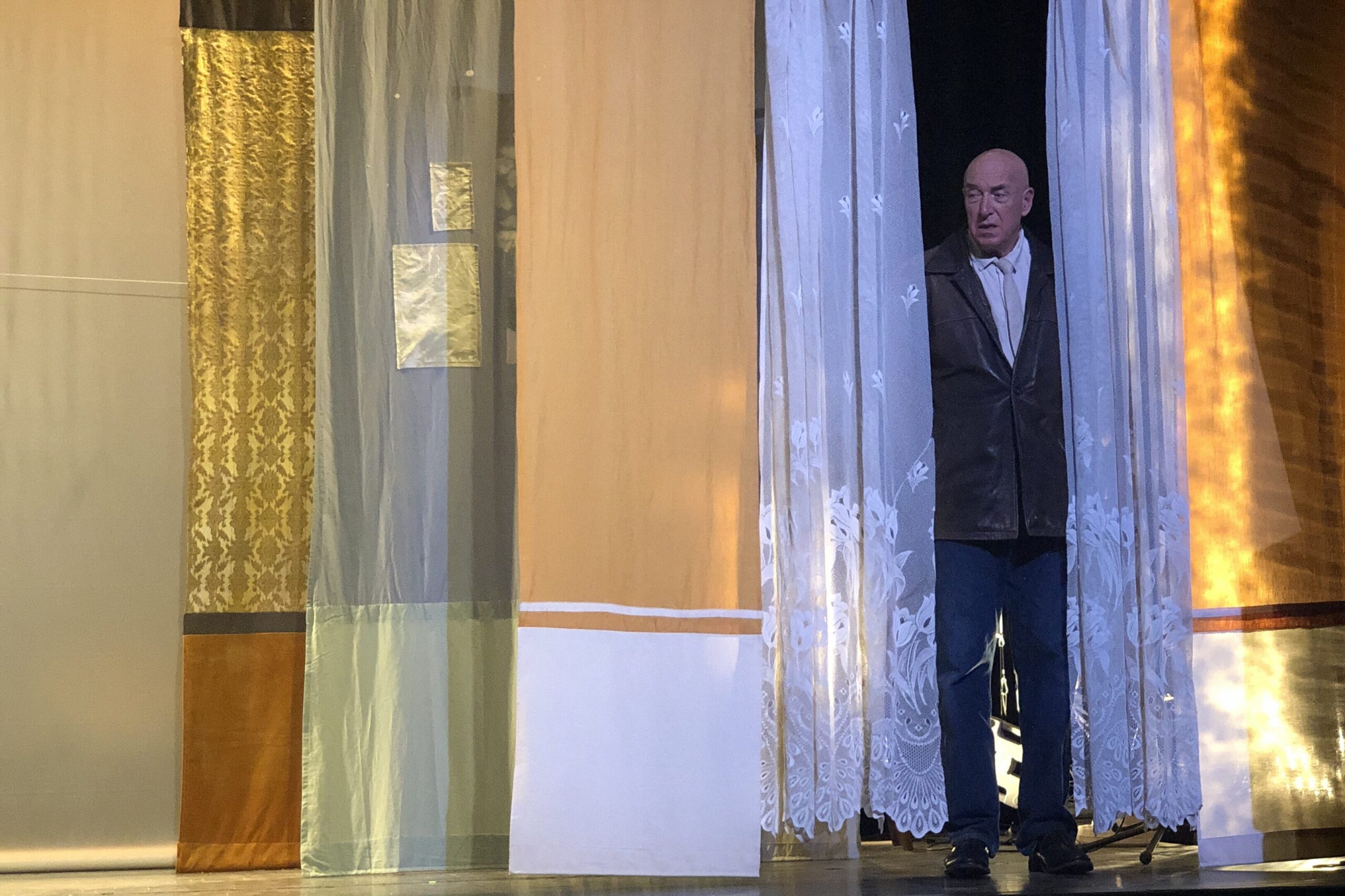 Le père à la fenêtre, dans le décors de la maison de famille représenté par des lés de tissus